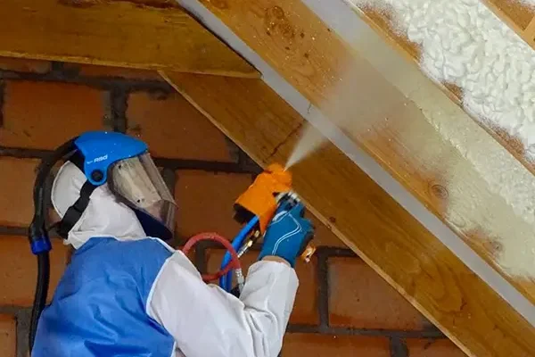 een expert in een wit en blauw pak die het plafond isoleert met spray-schuim