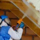 een expert in een wit en blauw pak die het plafond isoleert met spray-schuim