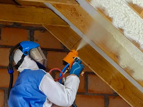 een expert in een wit en blauw pak die het plafond isoleert met spray-schuim