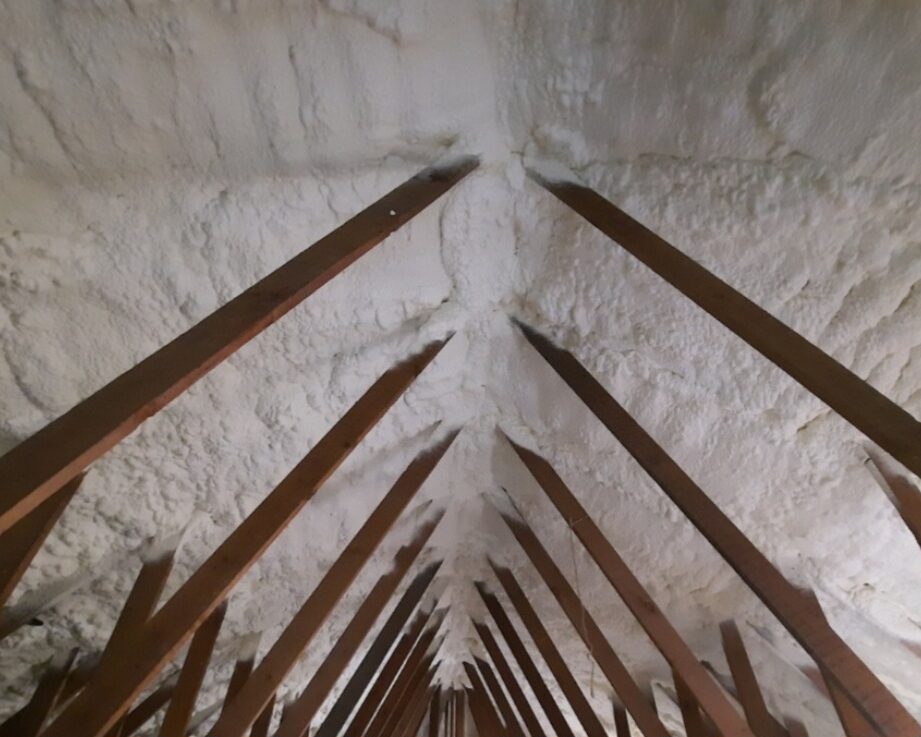 Intérieur d'une toiture d'une maison avec poutres en bois et mousse projetée pour l'isolation