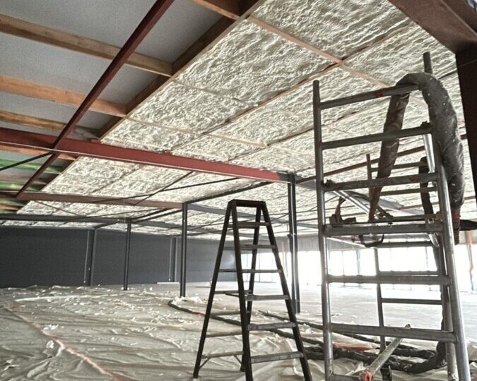 Application de mousse isolante sur le plafond d'un showroom de cuisines en construction à La Louvière, avec échafaudage et équipement de projection.