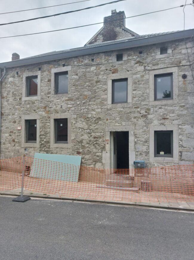 Façade en pierre d'une maison ancienne en rénovation à Grand-Rechain, avec des panneaux isolants visibles à l'avant-plan, préparés pour les travaux d'isolation.