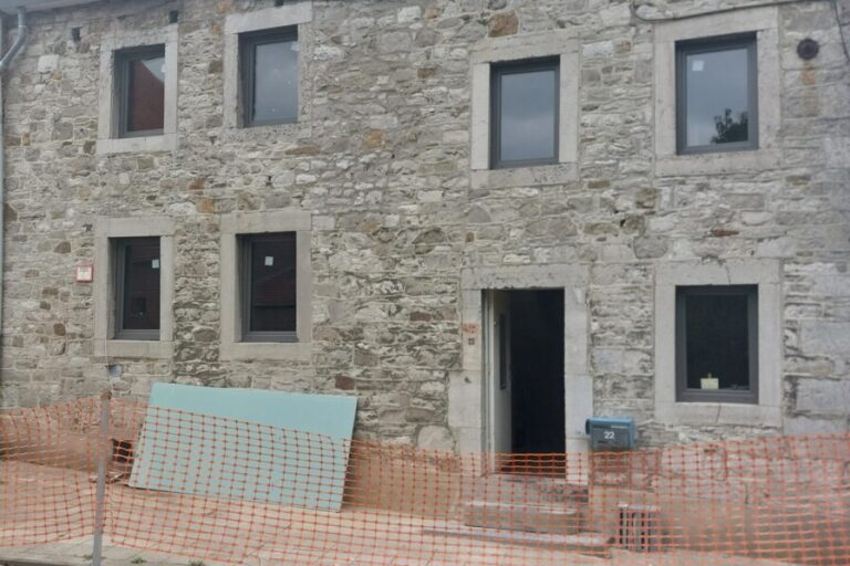 Façade en pierre d'une maison ancienne en rénovation à Grand-Rechain, avec des panneaux isolants visibles à l'avant-plan, préparés pour les travaux d'isolation.