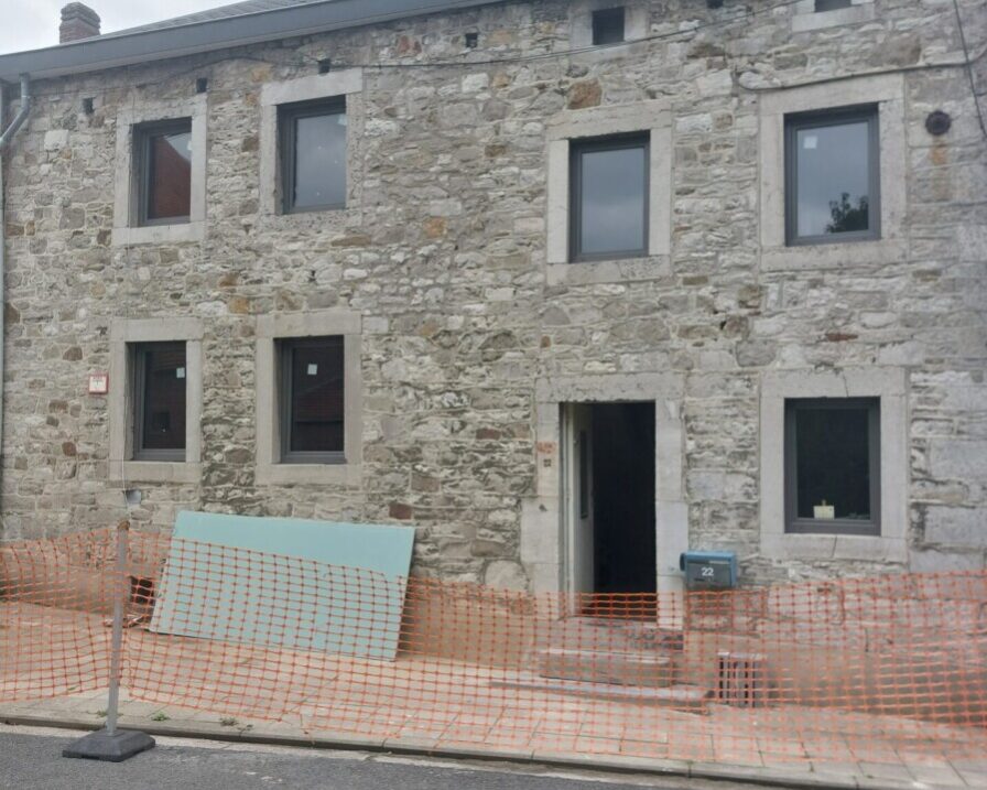 Façade en pierre d'une maison ancienne en rénovation à Grand-Rechain, avec des panneaux isolants visibles à l'avant-plan, préparés pour les travaux d'isolation.
