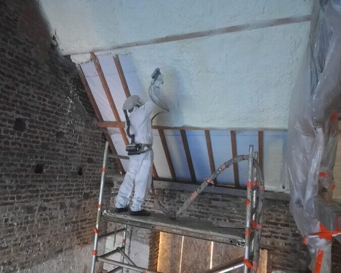 Ouvrier appliquant de la mousse polyuréthane projetée sur la toiture intérieure d'une grange en rénovation à Affligem.