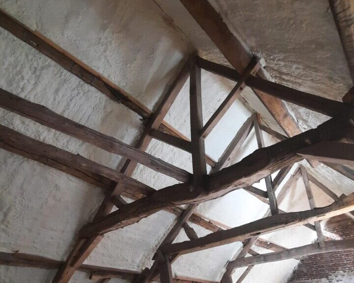 Isolation projetée à base de mousse sur le toit d'une grange à Affligem, avec protection des poutres en bois pendant les travaux.
