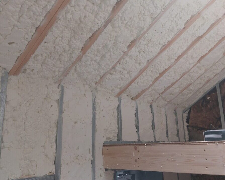 Détail de l'isolation en mousse projetée sous la toiture d'une maison ancienne à Grand-Rechain, mettant en avant les chevrons en bois visibles.