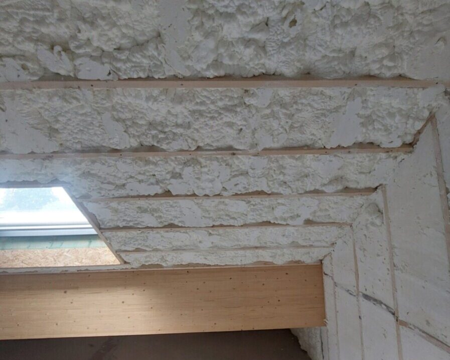 Plafond incliné isolé avec mousse projetée, les chevrons en bois sont visibles, et une grande fenêtre de toit éclaire naturellement la pièce en rénovation.