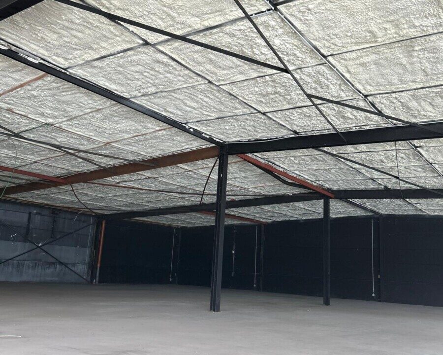 Vue intérieure d'un showroom avec une structure métallique apparente et un plafond entièrement recouvert de mousse isolante, dans un espace encore en travaux.
