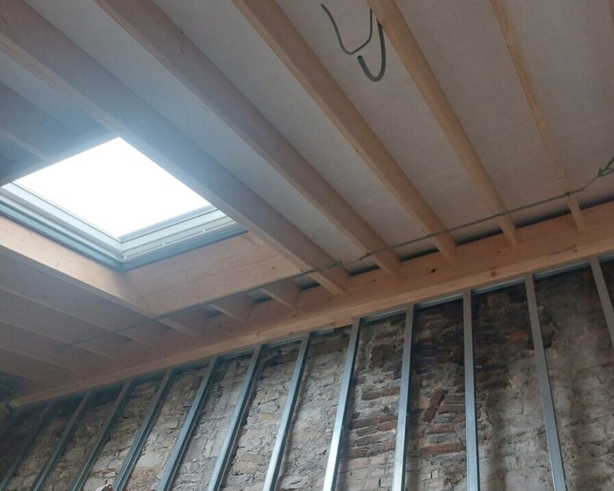 Isolation du plafond avec des panneaux sous les chevrons en bois et une fenêtre de toit dans une maison ancienne en rénovation.