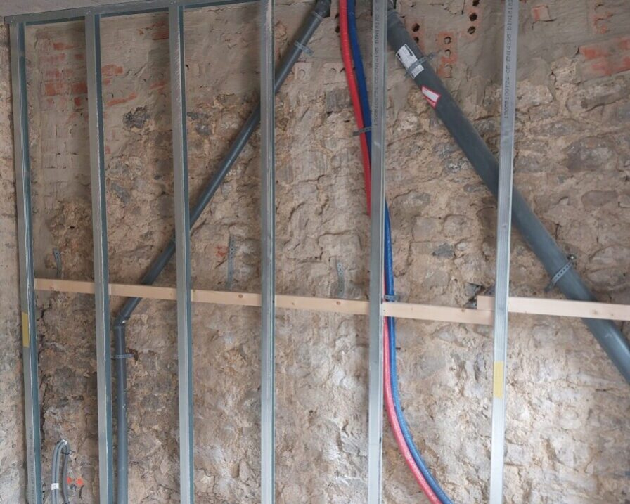 Structure métallique installée sur un mur en pierre dans une maison ancienne, préparée pour l'installation de l'isolation et du câblage électrique.
