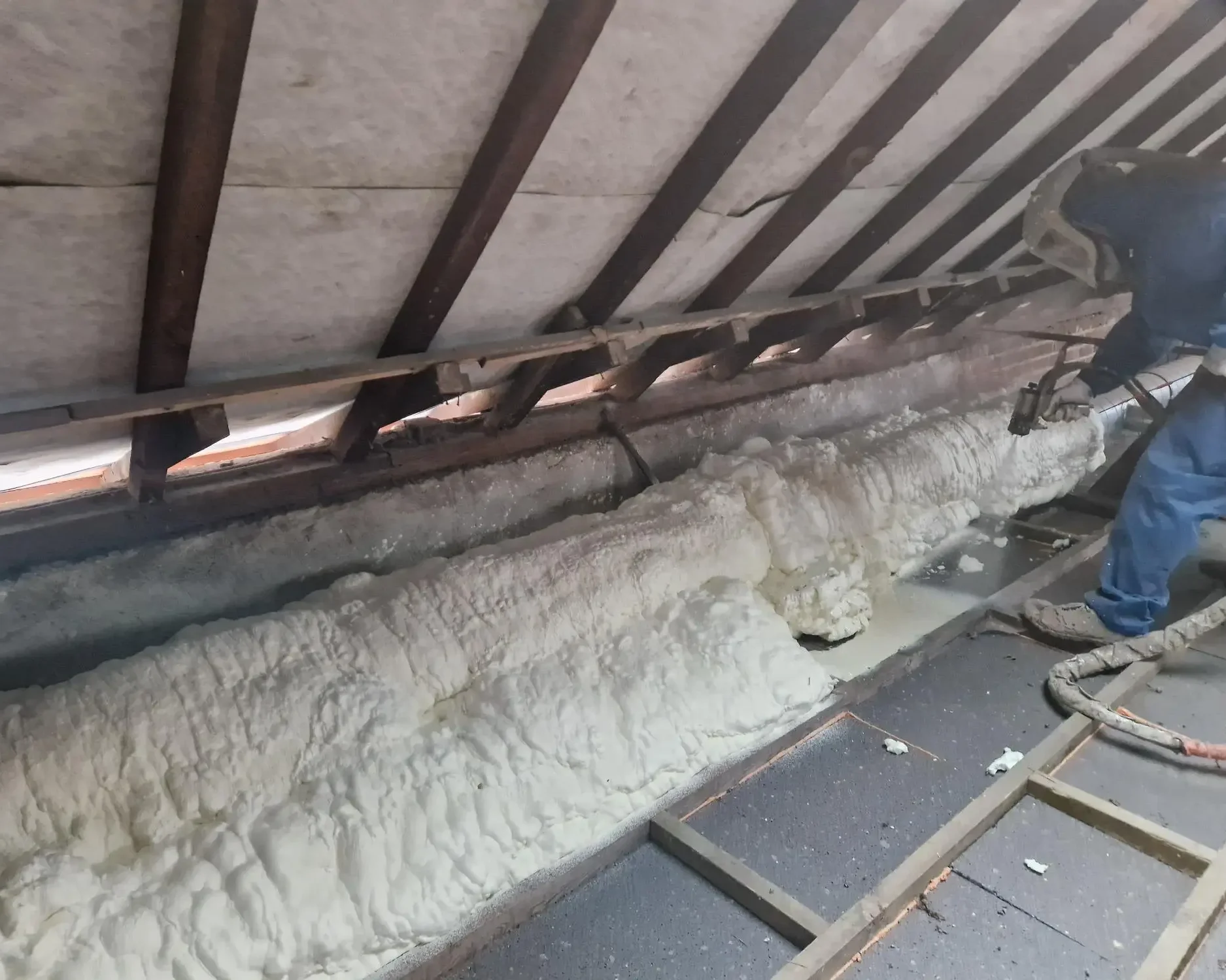 Application de mousse ICYNENE LITE+ par un expert dans le grenier à Destelbergen, assurant une isolation thermique et une étanchéité à l'air autour des structures et conduits.