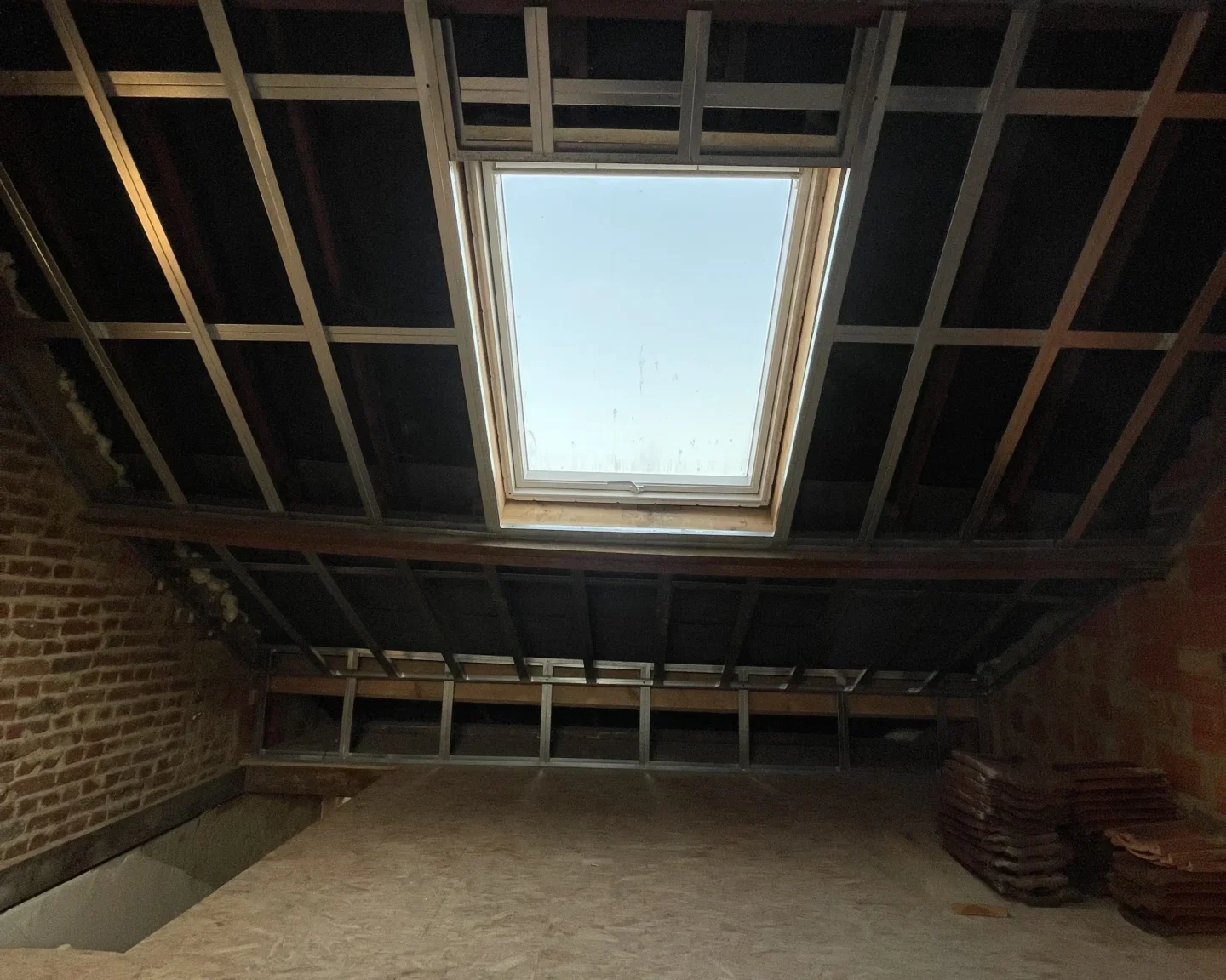 Structure de toiture en cours de préparation, avec une fenêtre de toit installée, avant l'isolation par mousse projetée à Tilly.