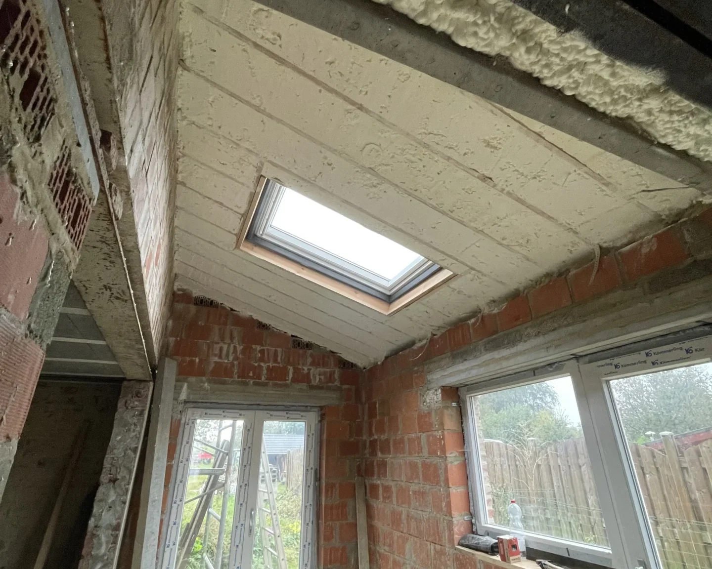 Réalisation d'une isolation de toiture avec mousse à cellules ouvertes, montrant une finition soignée autour d'une fenêtre de toit et des murs en cours de rénovation à Tilly.