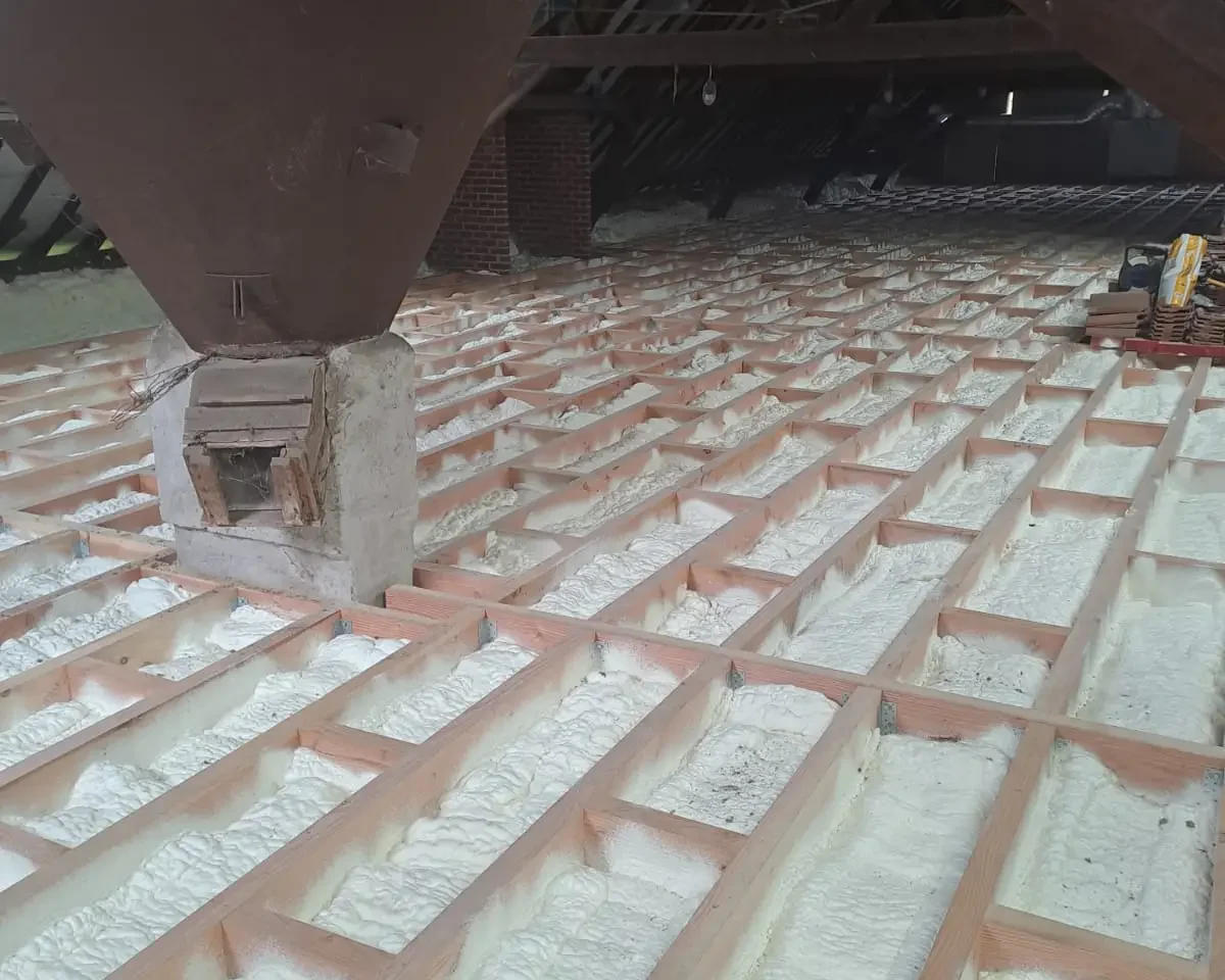 Plancher de grenier à Destelbergen isolé avec de la mousse ICYNENE LITE+ appliquée entre les poutres en bois, assurant une étanchéité à l'air et une isolation thermique efficace.