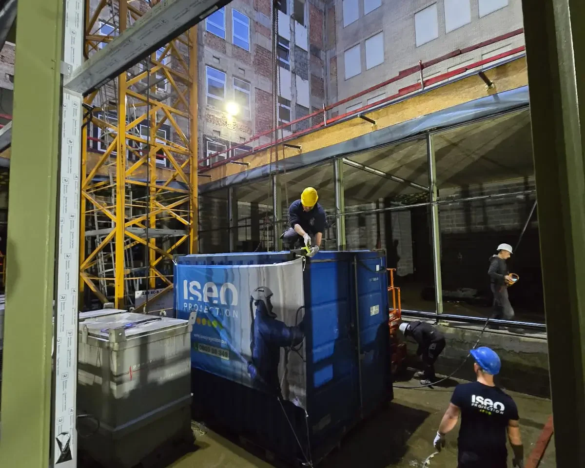 Manœuvre de l’unité de projection ISEO installée dans un conteneur sur le chantier d’isolation à Forest, avec intervention des équipes pour contourner les contraintes d’accès.