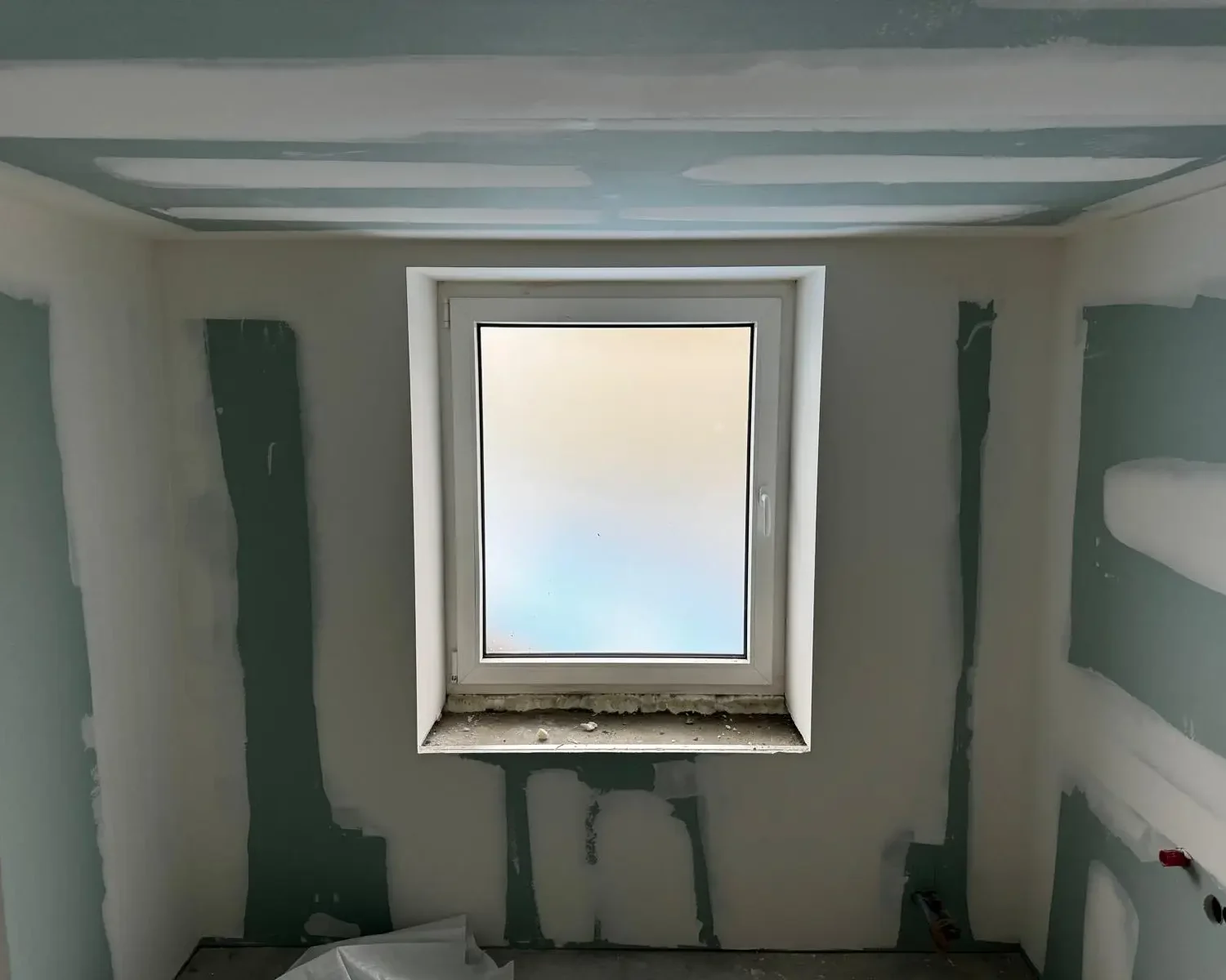 Travaux de parachèvement avec isolation thermique dans une pièce rénovée à Seilles, incluant finition des murs et plafond autour d’une fenêtre.