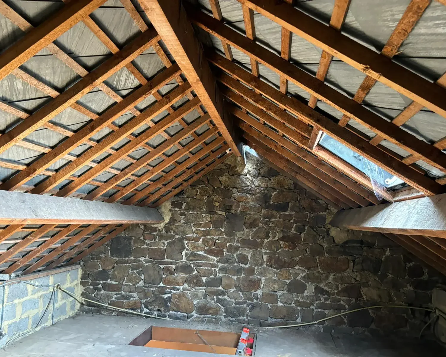 Combles avant isolation, avec charpente apparente et murs en pierre dans une habitation en rénovation à Seilles.