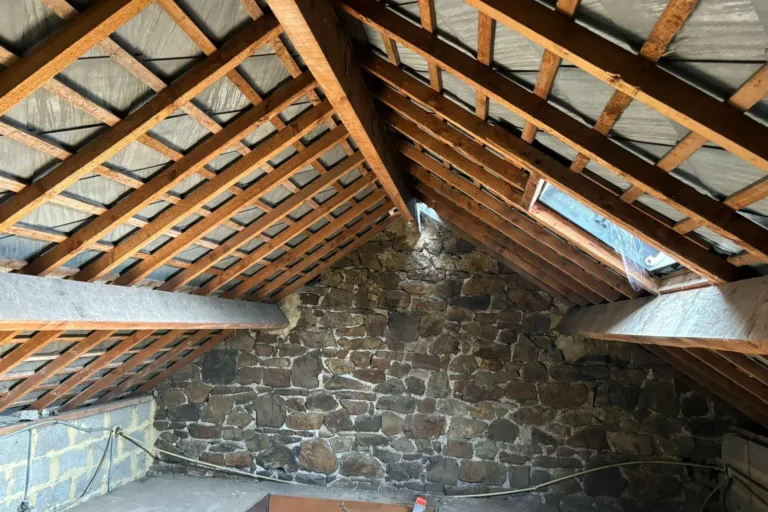 Combles avant isolation, avec charpente apparente et murs en pierre dans une habitation en rénovation à Seilles.