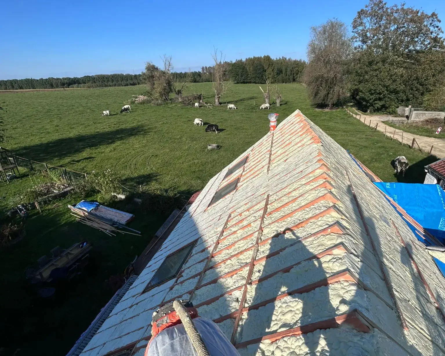Toiture en cours d’isolation par l’extérieur avec une sous-couche réfléchissante, sous un ciel bleu, dans un cadre rural.