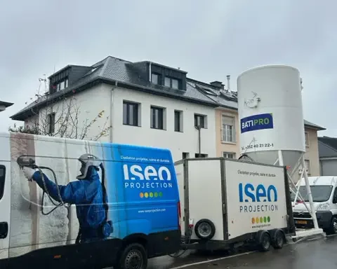 Camion et matériel d'ISEO Projection stationnés devant un bâtiment en cours d’isolation à Howald. L’équipement professionnel permet l’application de mousse projetée pour une isolation thermique optimale.
