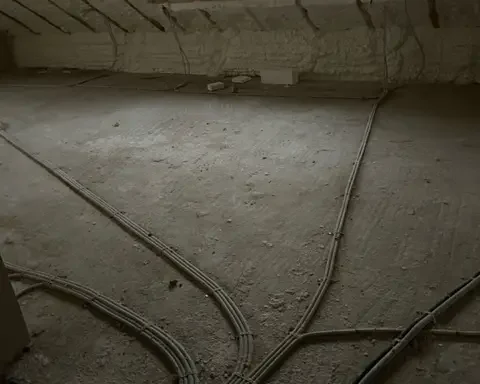 Vue intérieure d’un grenier en cours de rénovation à Howald, avec isolation en mousse projetée sur la toiture et préparation du sol avec installation de gaines techniques.