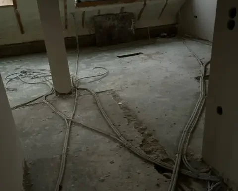 Vue intérieure d’un grenier en cours de rénovation à Howald, avec isolation en mousse projetée sur la toiture et préparation du sol avec installation de gaines techniques.