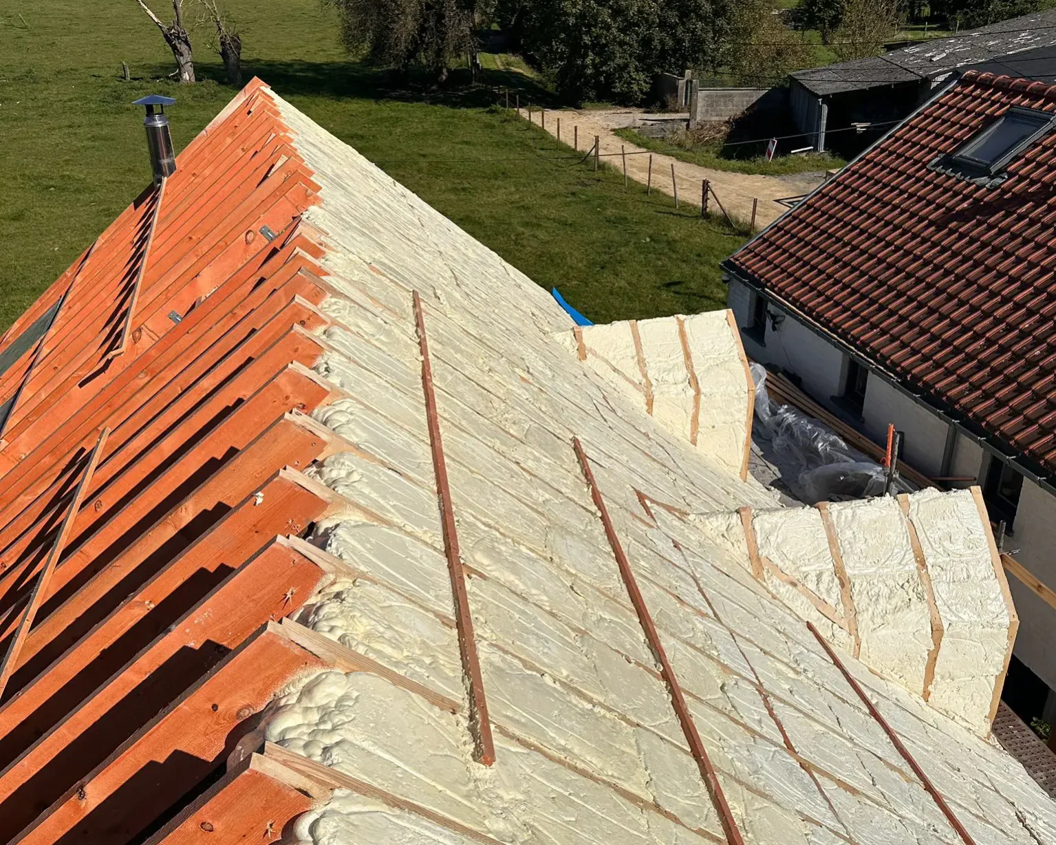 Toiture isolée par l’extérieur avec de la mousse projetée, avant la pose des tuiles, dans un environnement rural ensoleillé.