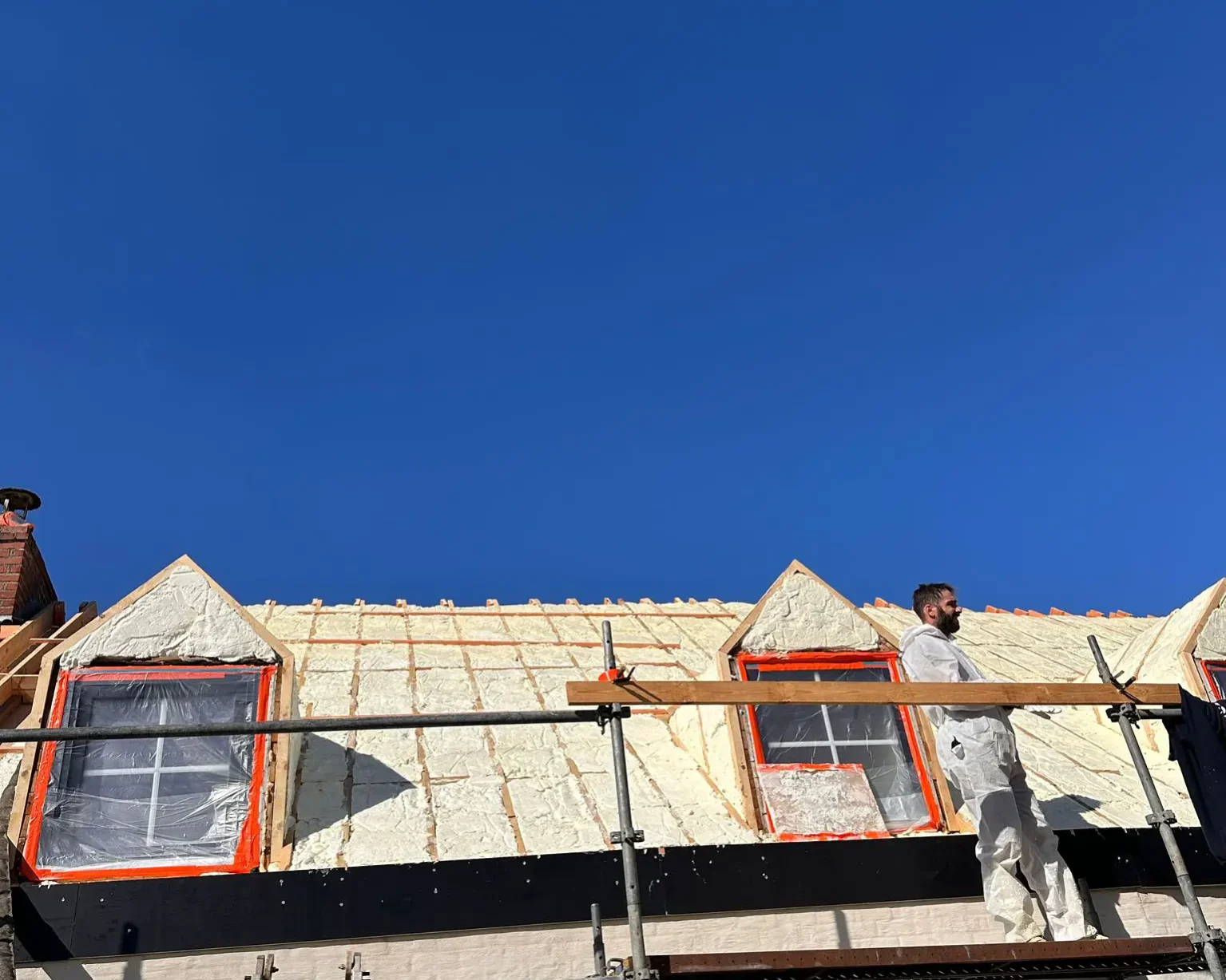 Isolation thermique d’une toiture par l’extérieur avec mousse projetée, intervention en cours sur un chantier avec échafaudage.