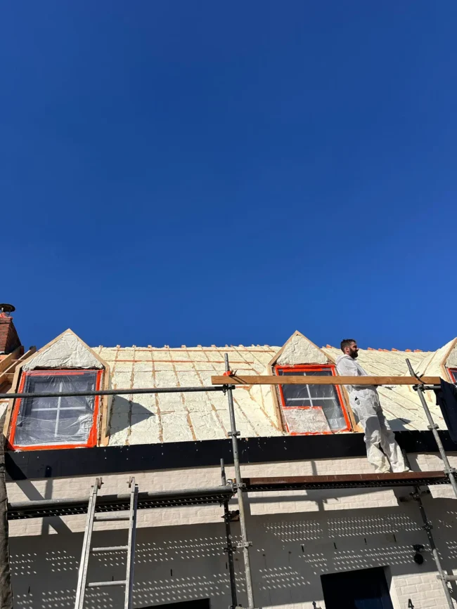 Isolation thermique d’une toiture par l’extérieur avec mousse projetée, intervention en cours sur un chantier avec échafaudage.