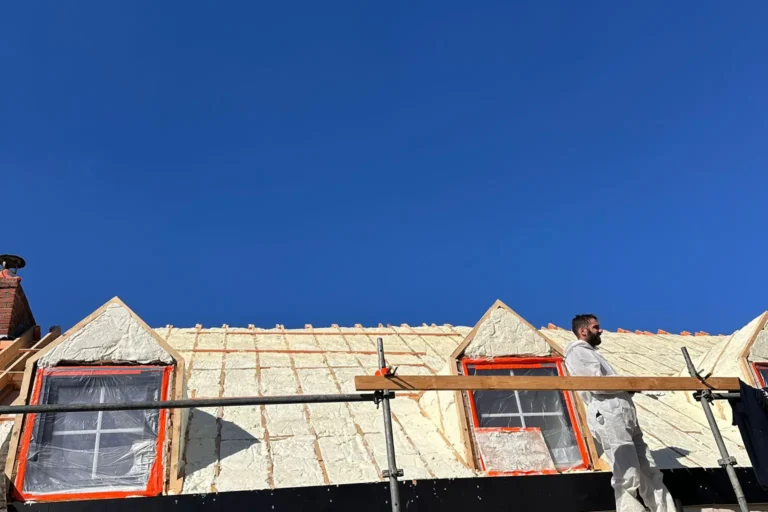 Isolation thermique d’une toiture par l’extérieur avec mousse projetée, intervention en cours sur un chantier avec échafaudage.