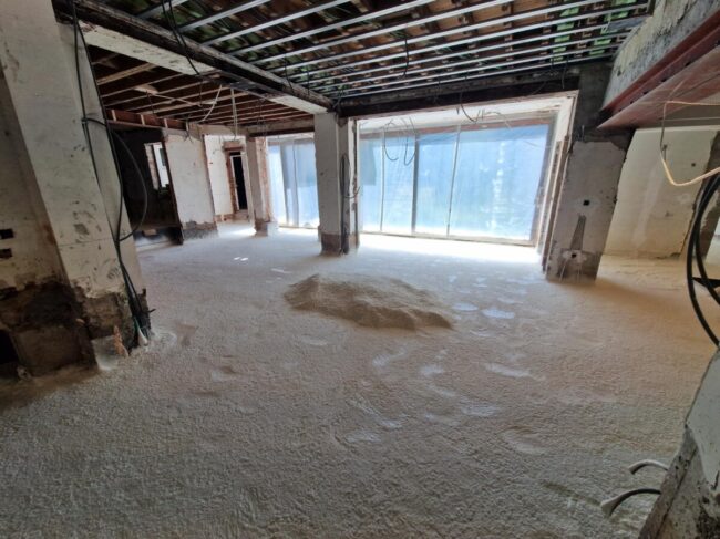 Vue d'un salon en travaux avec le sol recouvert d'isolant par mousse projetée