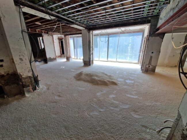 Vue d'un salon en travaux avec le sol recouvert d'isolant par mousse projetée