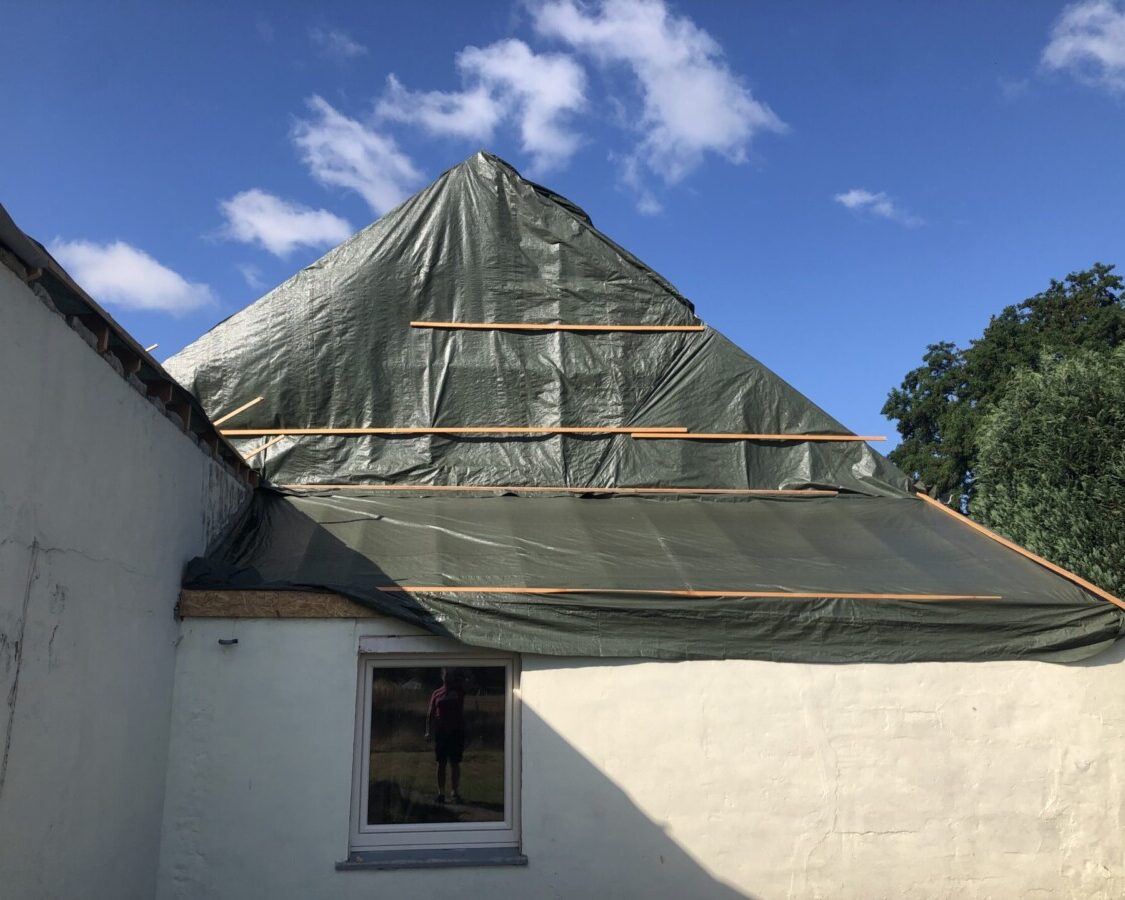 Pignon extérieur d'une maison blanche recouverte d'une bâche lors de travaux d'isolation