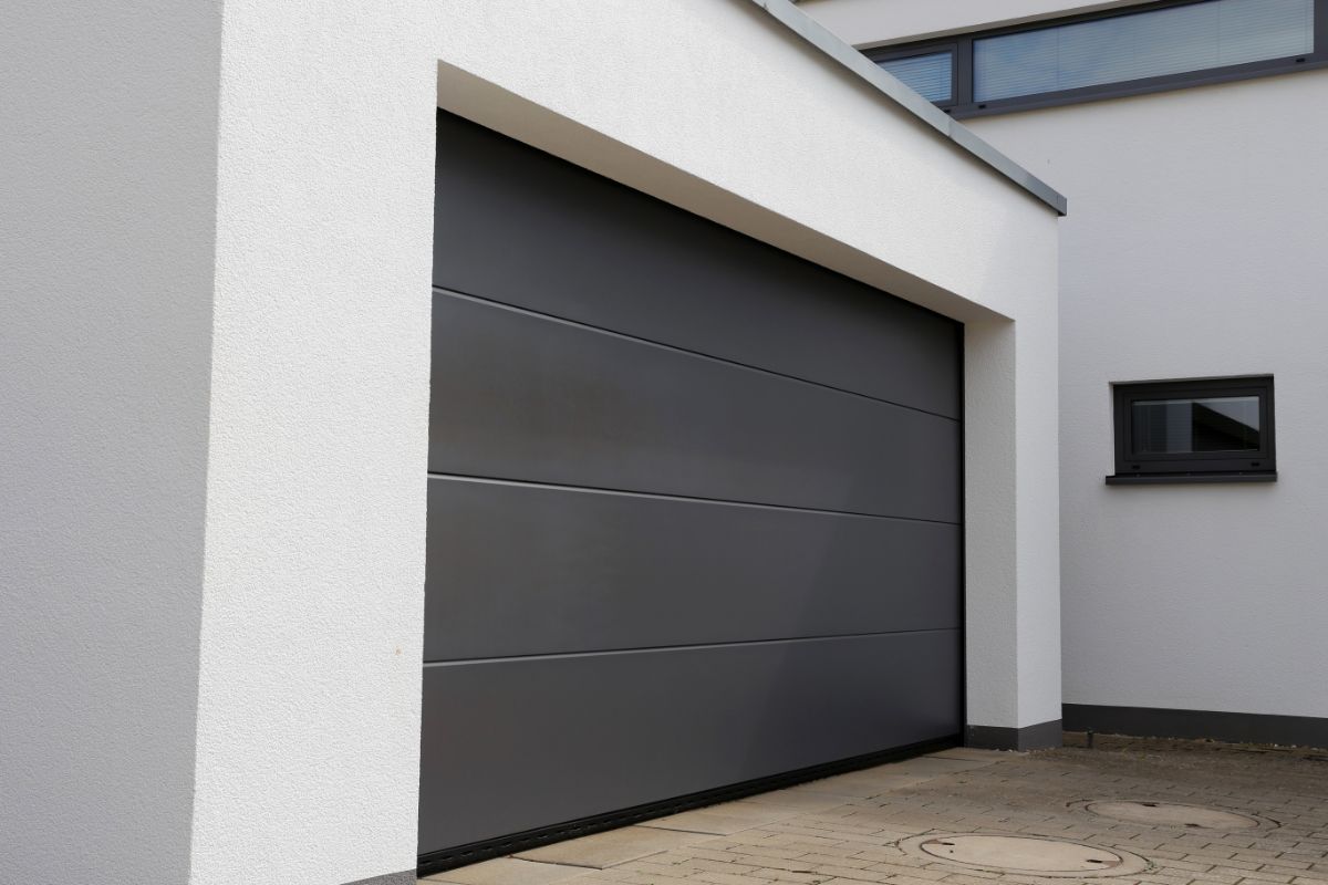 Garage d'une maison moderne en crépi blanc avec une porte sectionnelle gris foncé