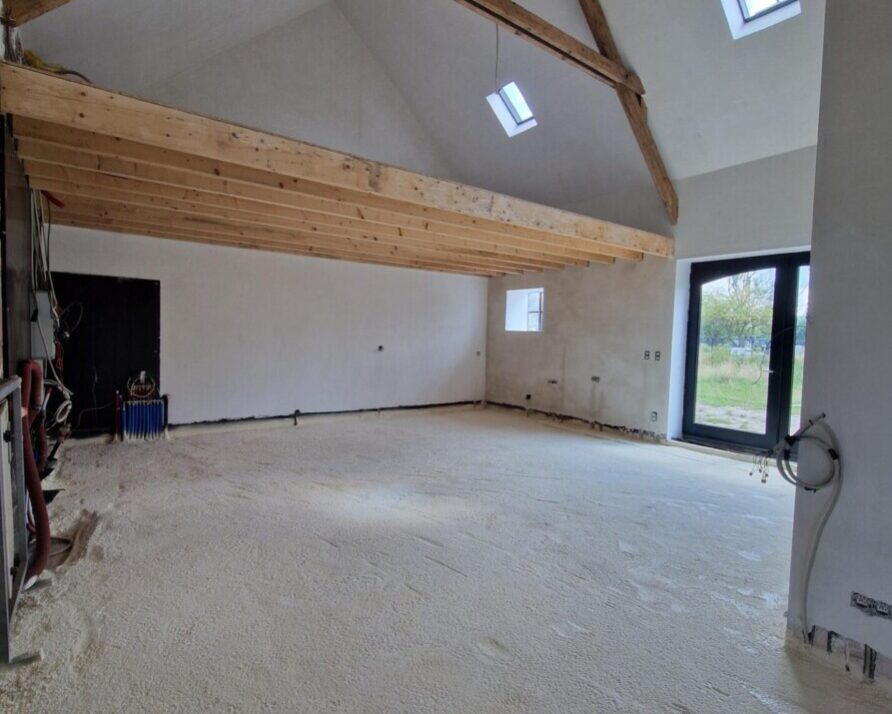 Intérieur d'une ferme que l'on rénove avec murs blancs, poutres en bois et sol recouvert de mousse isolante