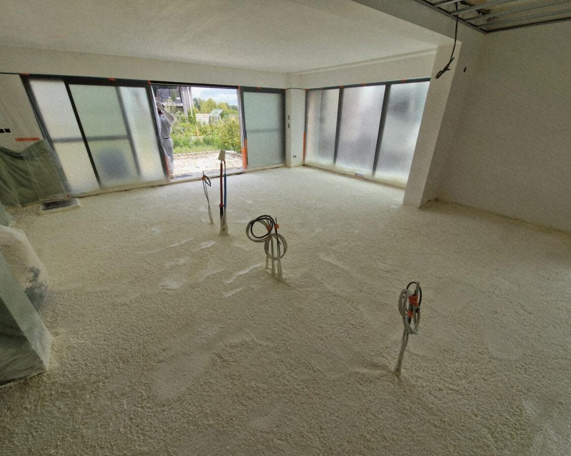 Vue sur le futur salon d'une maison en construction avec le sol recouvert de mousse projetée