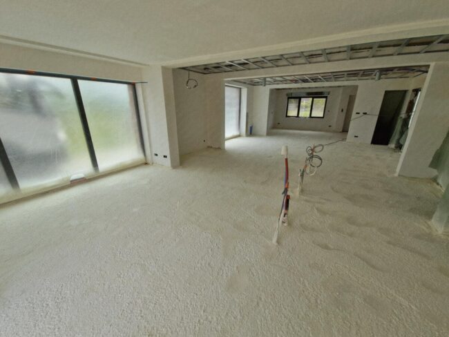 Living d'une maison neuve dont le sol est recouvert de mousse isolante projetée