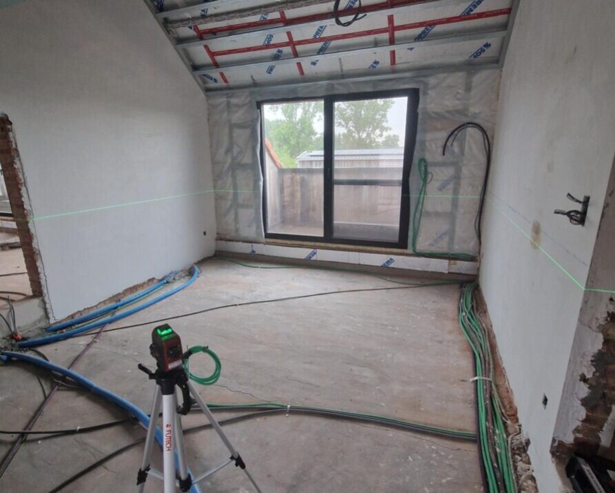 Intérieur d'une maison en chantier avec des câbles sur le sol et un instrument de mesure en premier plan