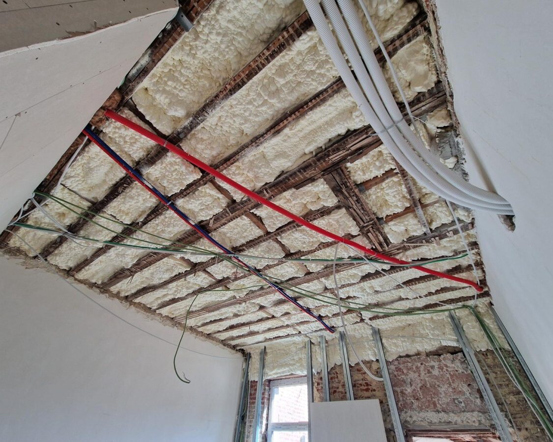 Isolation de plafond et de toiture à la mousse H2O projetée dans une maison en rénovation complète à Zaventem : gaines électriques et de plomberie intégrées avant projection.