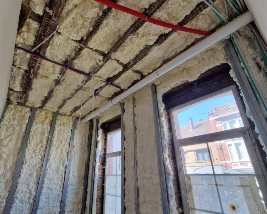 Vue d'ensemble de l'isolation complète d'une maison à Zaventem : mousse projetée H2O sur murs (12 cm) et plafond (12 cm), réseau de gaines et menuiseries extérieures posées.