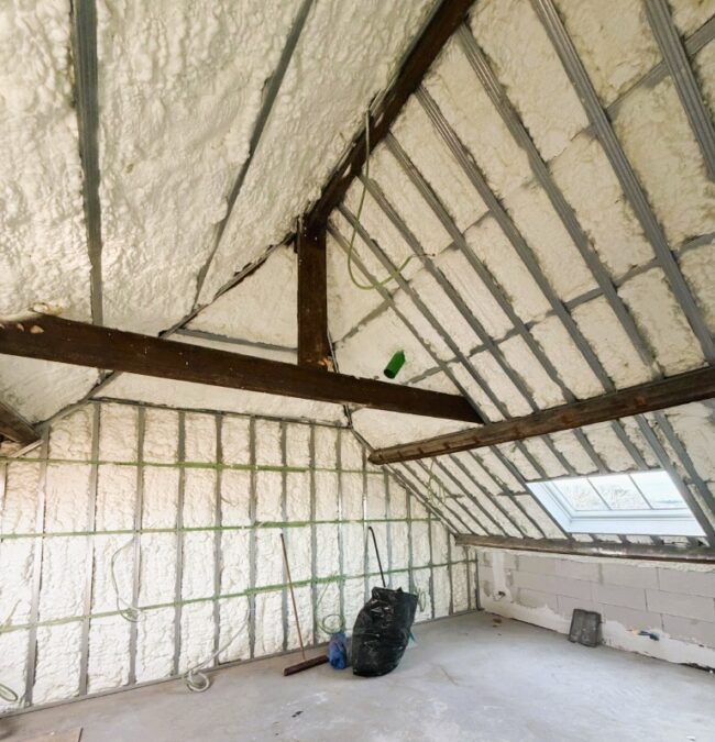 
Isolation de la toiture inclinée d'un grenier à Zaventem avec 17 cm de mousse polyuréthane H2O projetée : chevrons apparents, ossature métallique et fenêtre de toit.