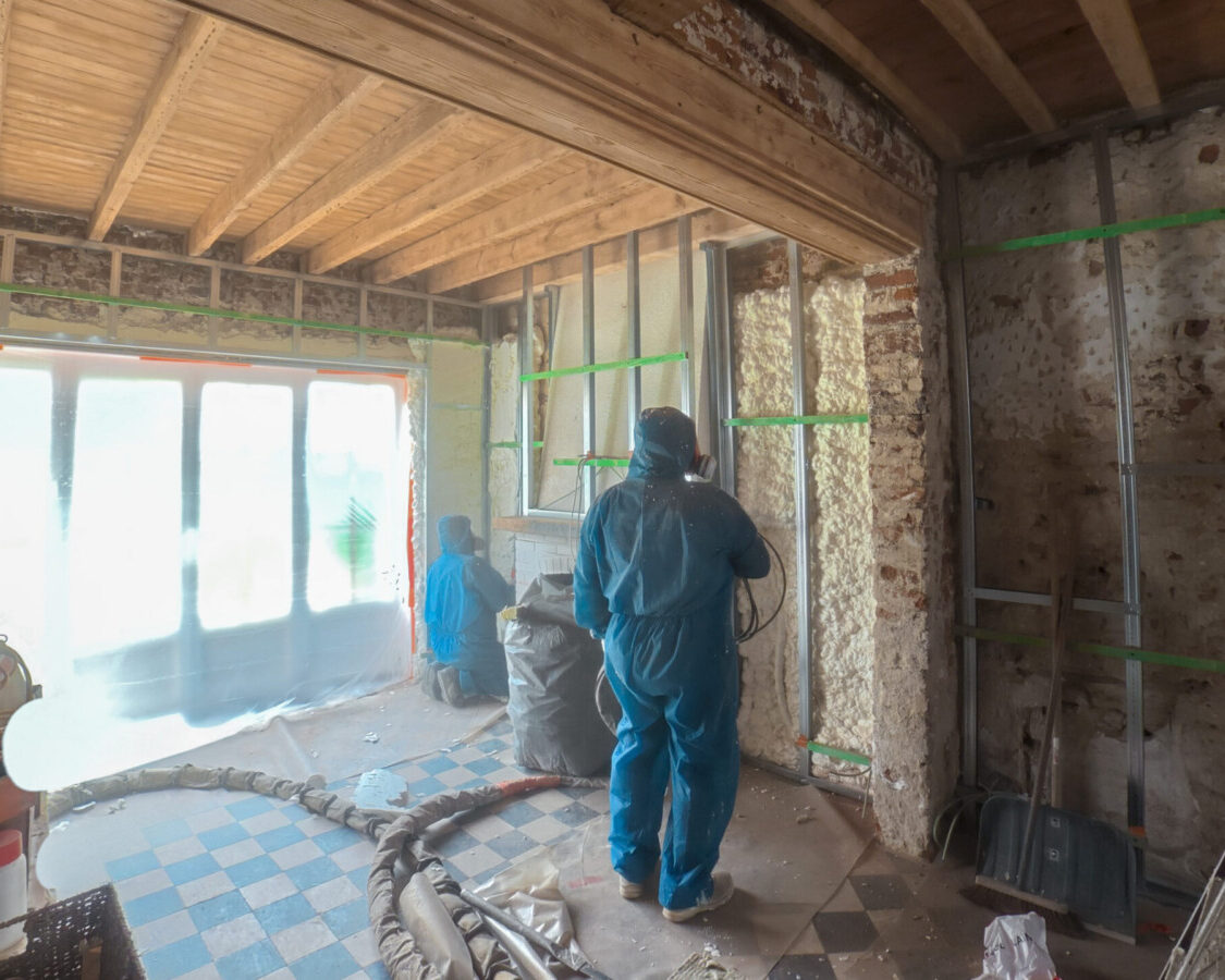 Techniciens ISEO Projection réalisant l’isolation intérieure d’une fermette à Braives par projection de mousse polyuréthane sur des murs anciens en briques.