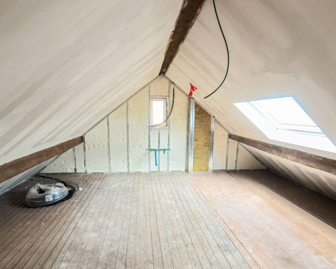 Combles rénovés avec isolation performante sous toiture, murs isolés à la mousse polyuréthane projetée et fenêtre de toit apportant la lumière naturelle.