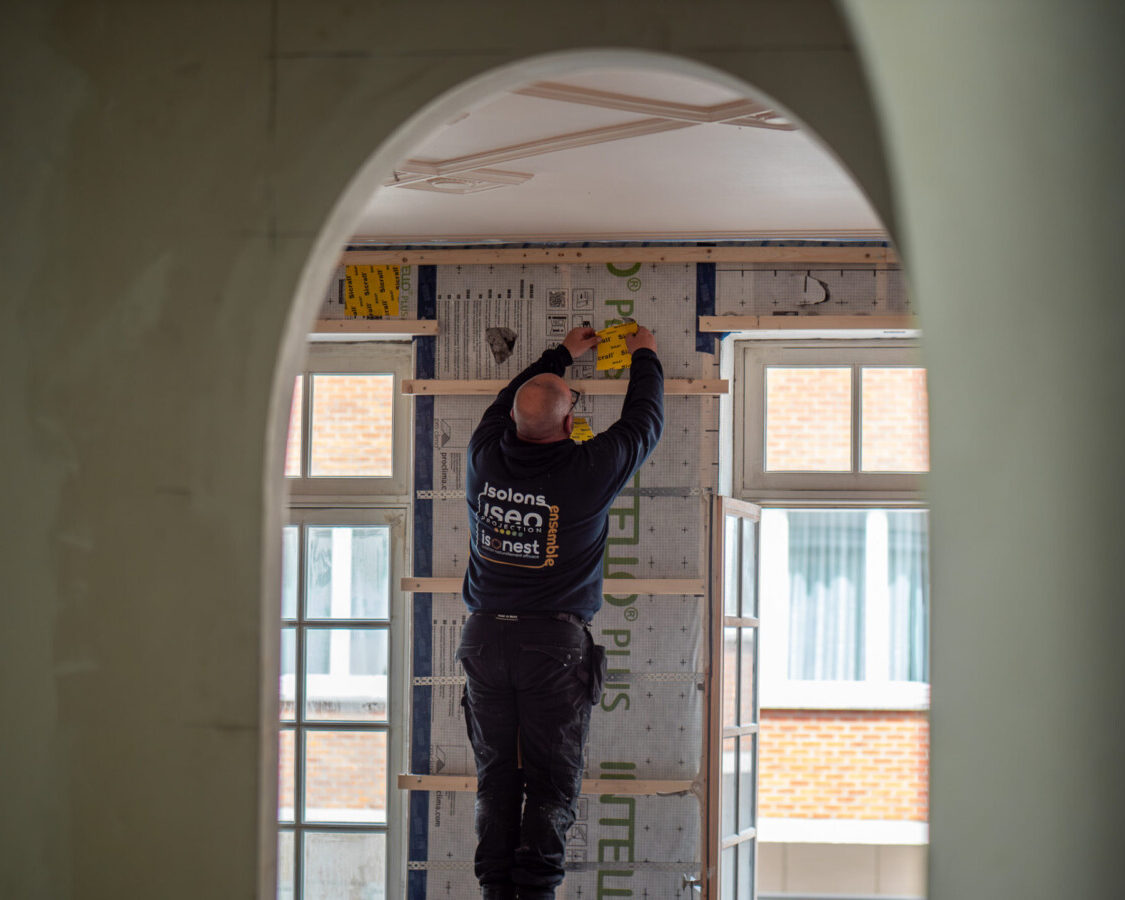 Technicien réalisant les finitions d’un mur isolé par insufflation de ouate de cellulose dans un appartement en rénovation à Etterbeek.